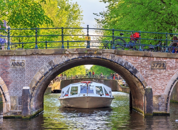 Canal cruise boat goes under the bridge over the Leidse canal at the Patricians' or Lords' canal (Herengracht) in Amsterdam in spring
