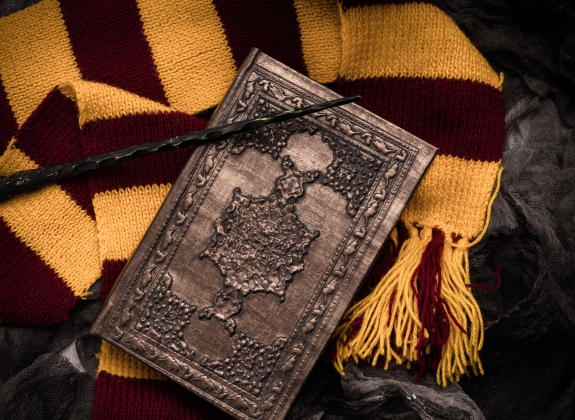 Subjects of the school of magic. Scarf, magic wand, book of spells on grey dark rag background.