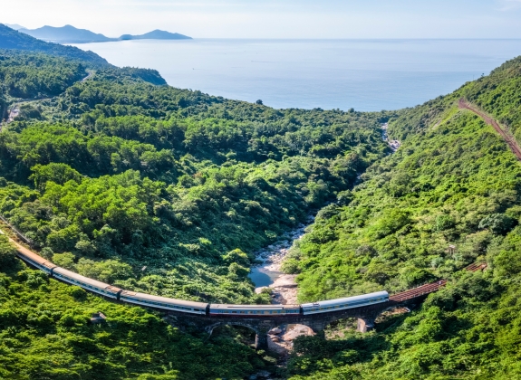 A train travels through lush landscape with coast on horizon