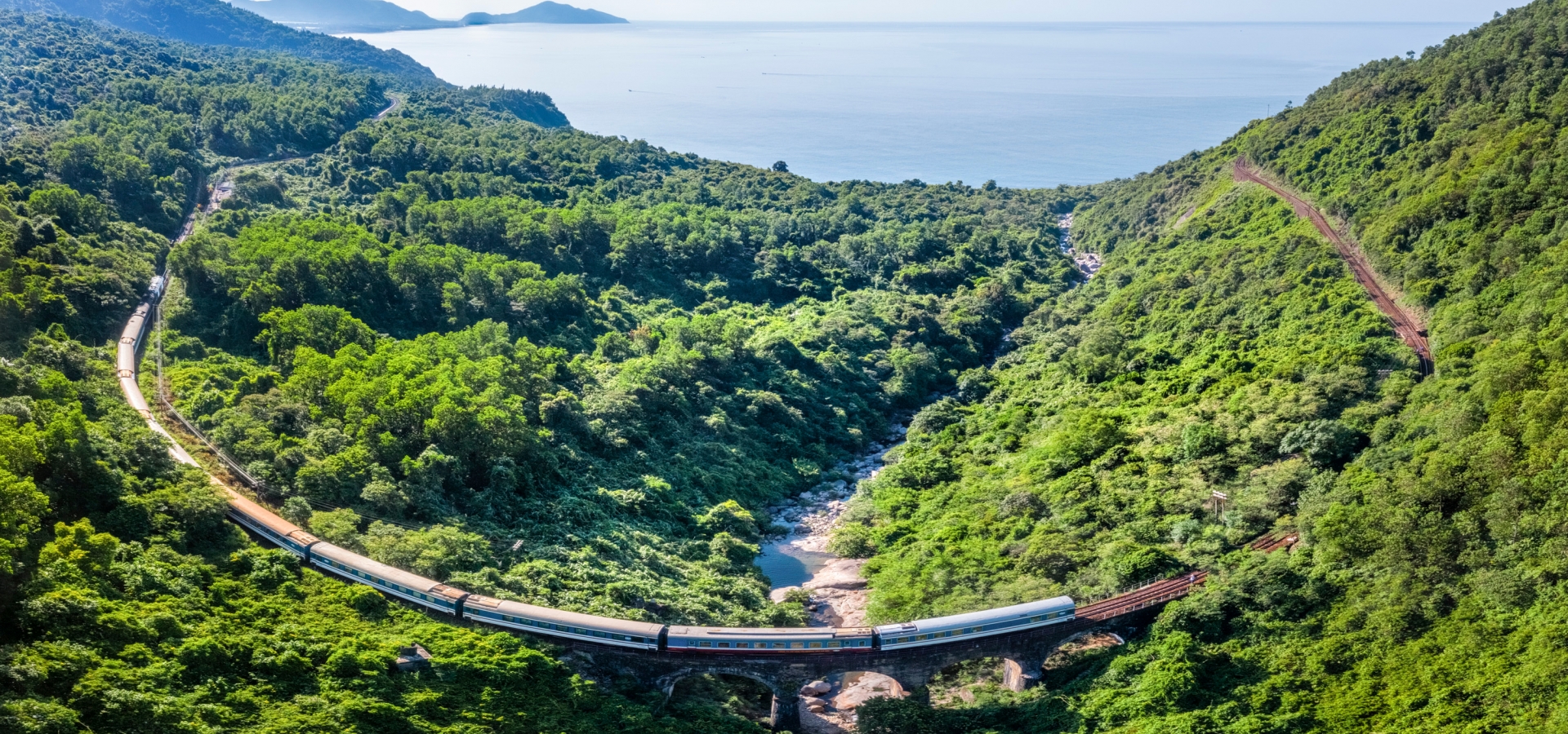 A train travels through lush landscape with coast on horizon