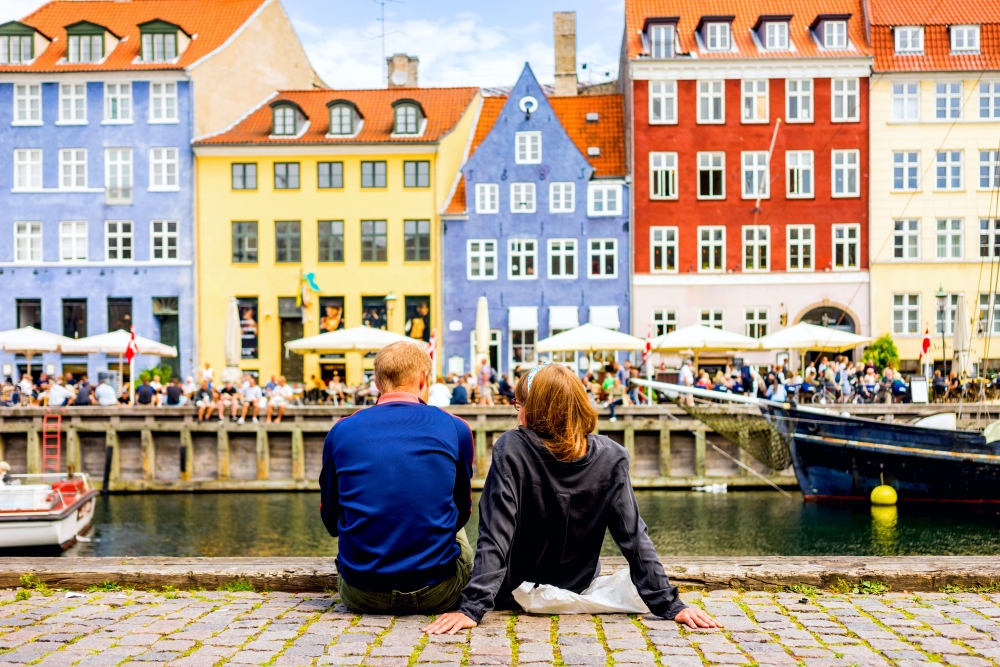 Tourists enjoying the scenic summer view of Nyhavn pier. Colorful building facades with boats and yachts in the Old Town of Copenhagen, Denmark